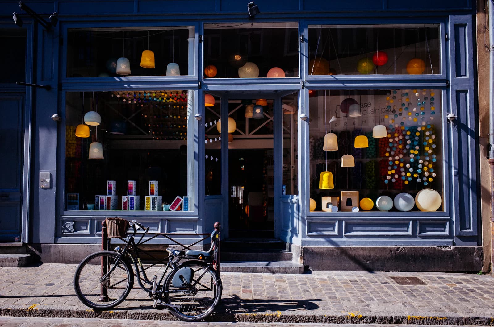 Independent shop front with lamps in the windows and a bicycle parked outside on a cobbled street