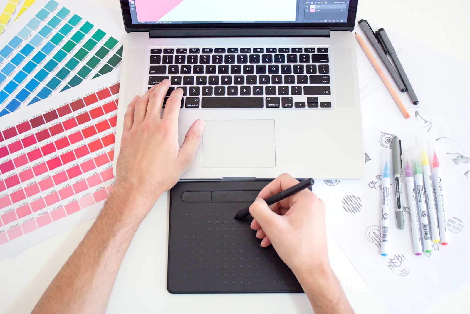 Designer using a drawing tablet beside a laptop and printed colour swatches
