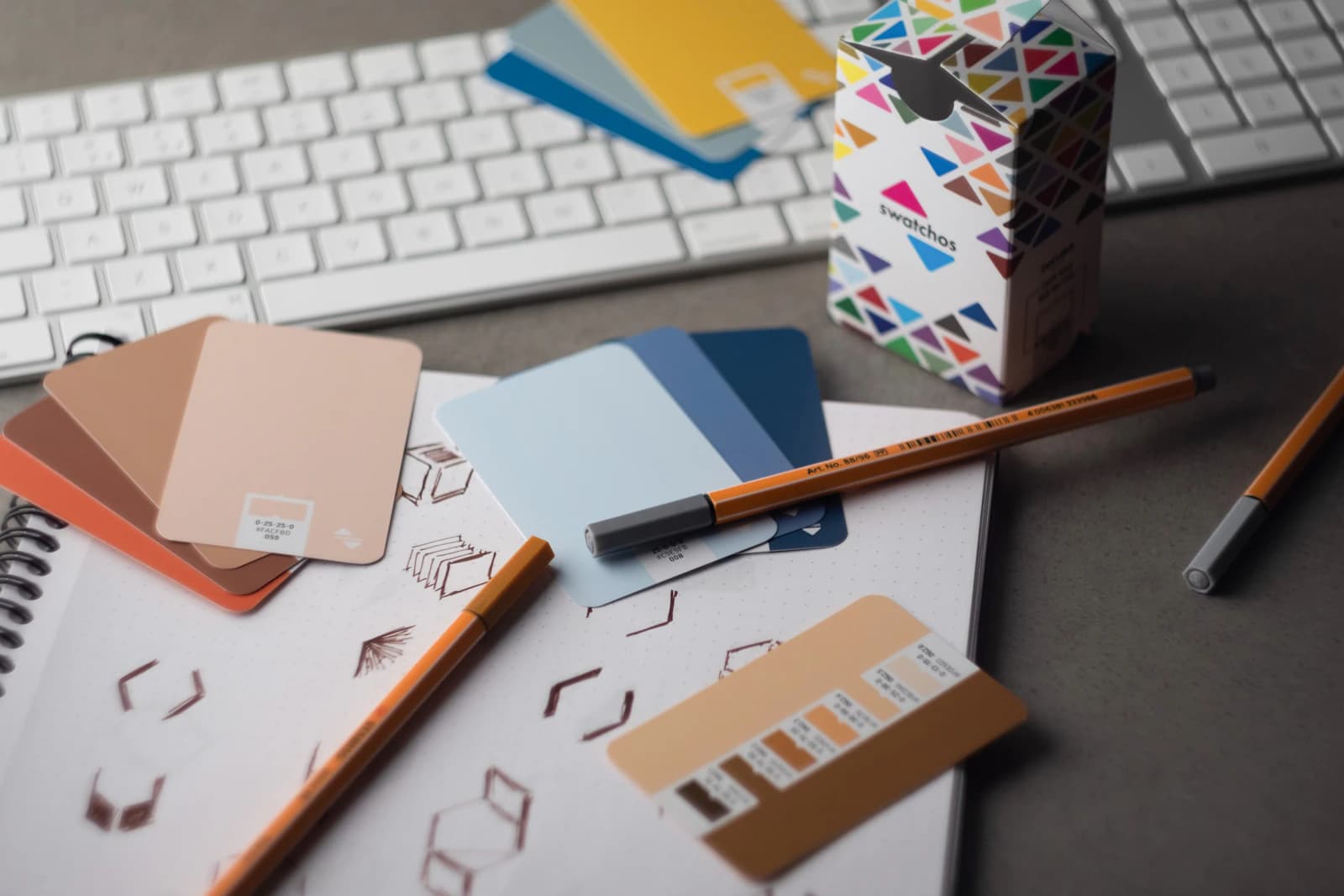 Colour swatch cards, pens and logo sketches spread across a designer's desk