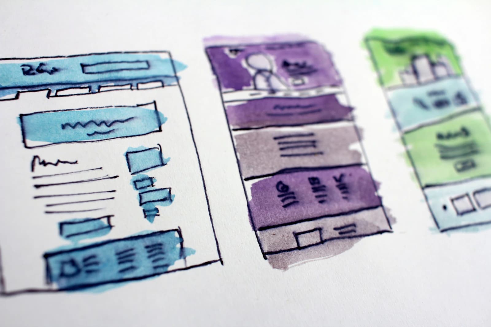 Watercolour wireframe sketches of three website page layouts on white paper