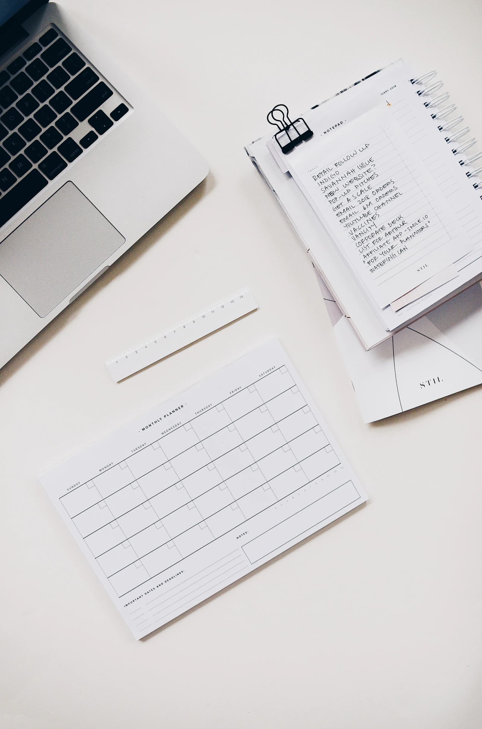 Laptop beside a handwritten task list and a monthly planner on a white desk