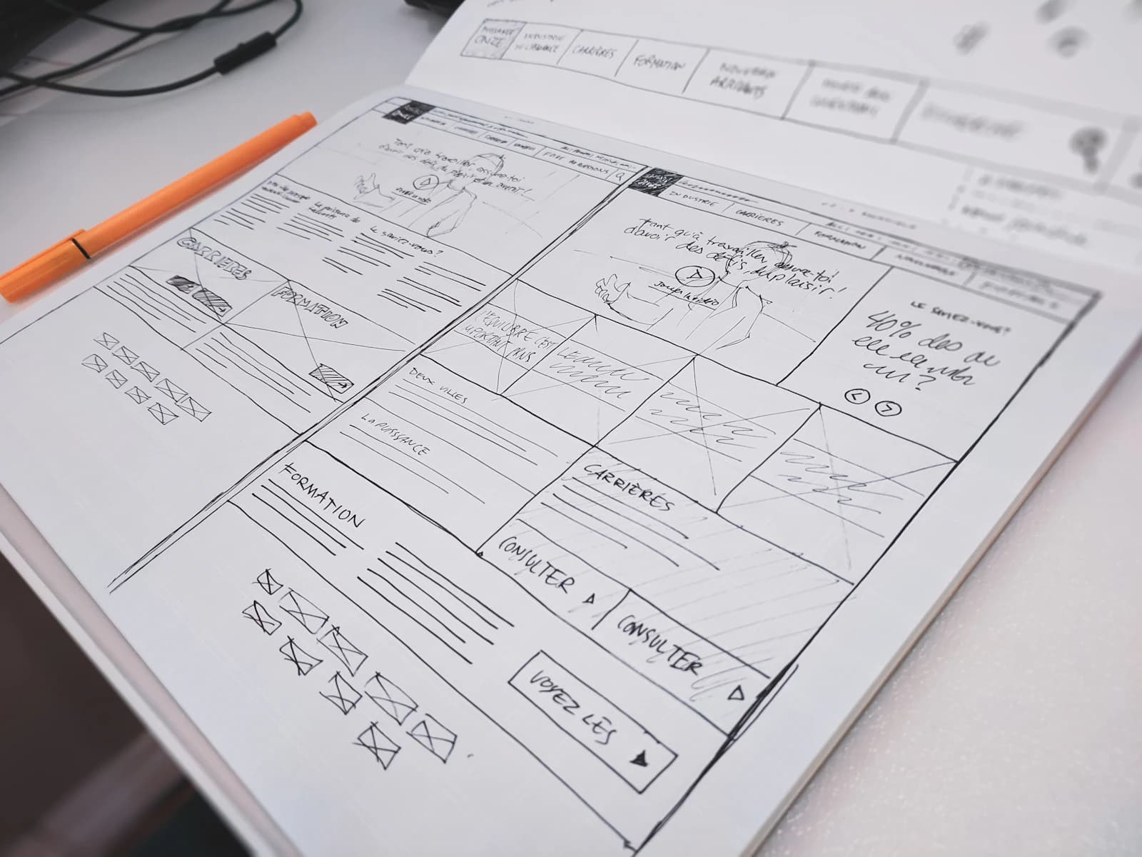 Hand-drawn website wireframe sketches in a notebook next to an orange pen