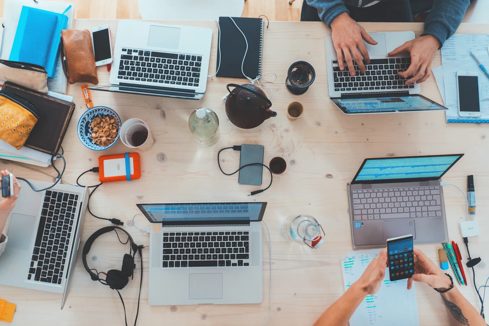 Overhead view of a shared desk with several laptops, notebooks and phones as a team works together