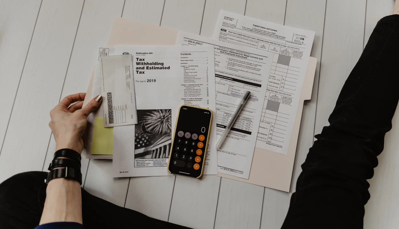 Person reviewing printed figures with a pen and calculator on a desk