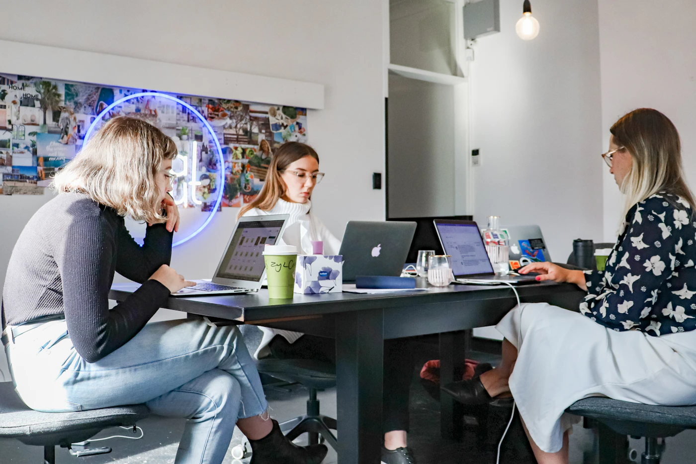 Three colleagues working on laptops around a shared table in a bright studio