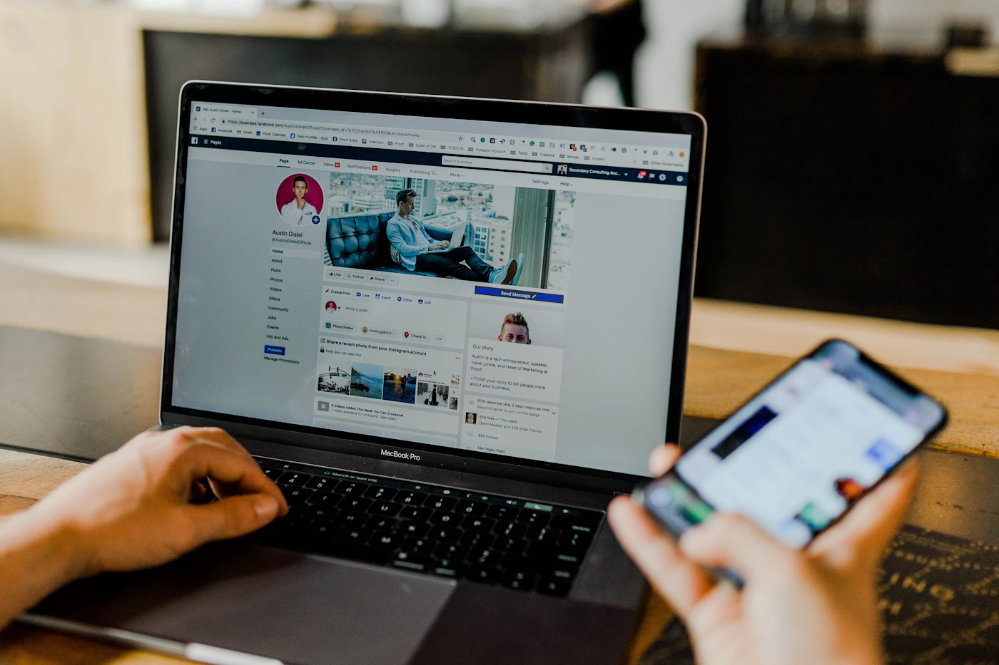 Hands on a laptop showing a Facebook business page while holding a phone