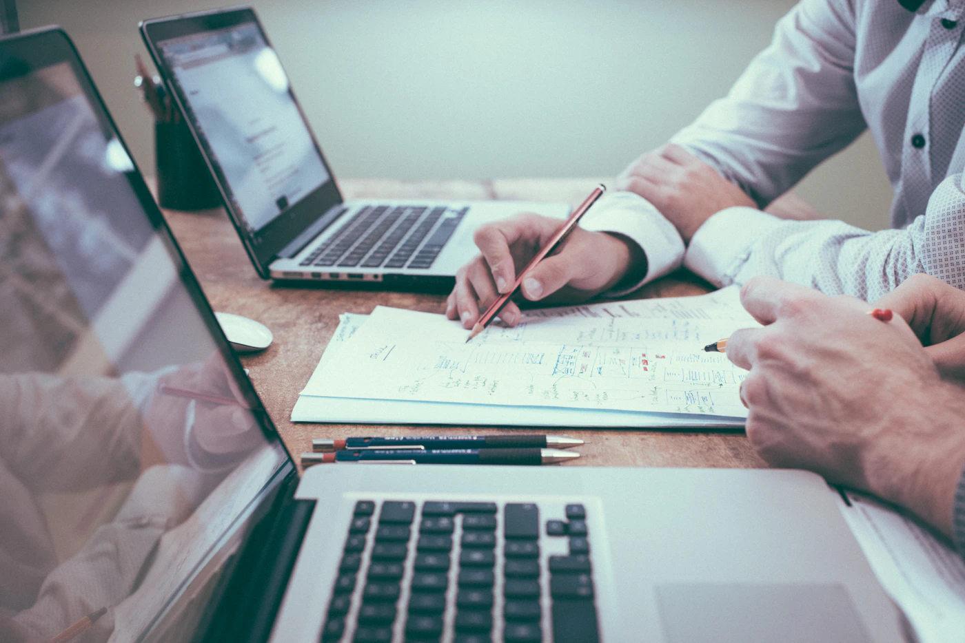 Two people reviewing printed website plans beside laptops on a wooden desk