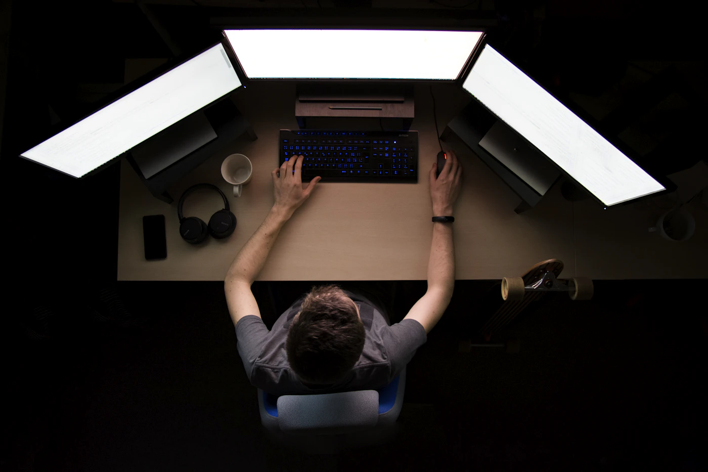 Developer working at a desk with three large monitors in a dark room