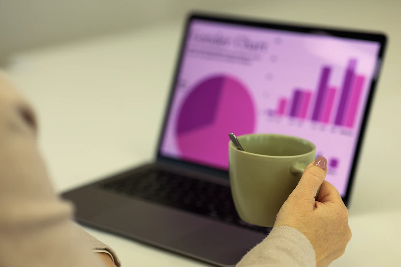 Person holding a mug in front of a laptop displaying colourful bar and pie charts